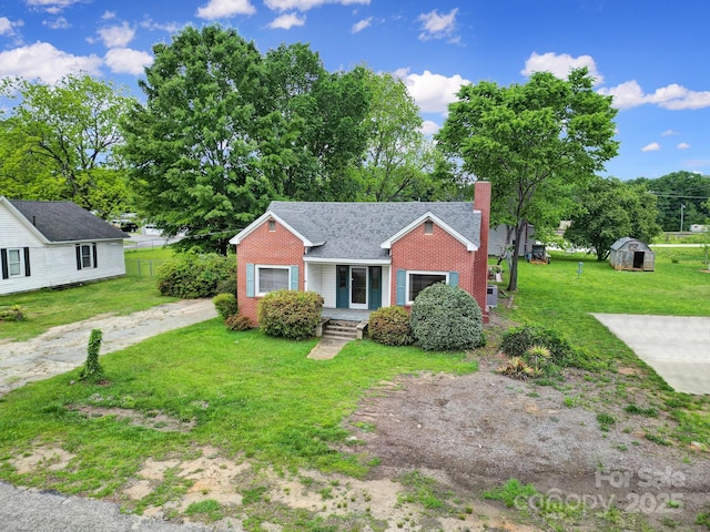 bungalow-style house featuring a chimney, a front yard, brick siding, an outdoor structure, and a storage unit