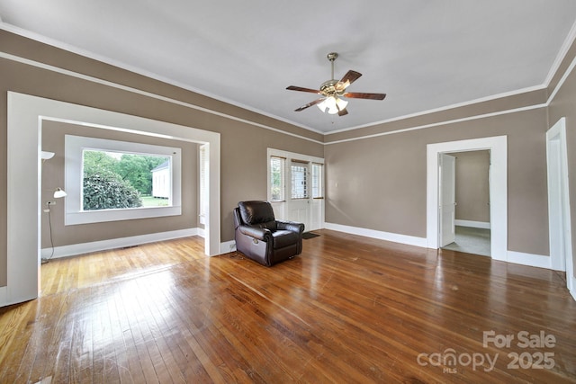 living area featuring crown molding, a ceiling fan, baseboards, and wood-type flooring
