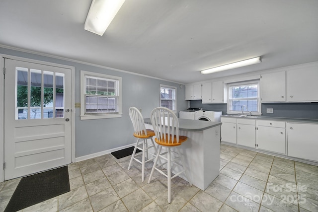 kitchen with ornamental molding, white cabinetry, independent washer and dryer, and a healthy amount of sunlight