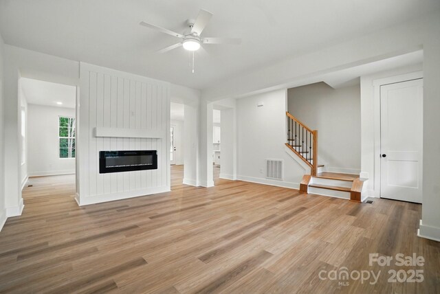 unfurnished living room featuring visible vents, stairs, baseboards, light wood-style floors, and ceiling fan