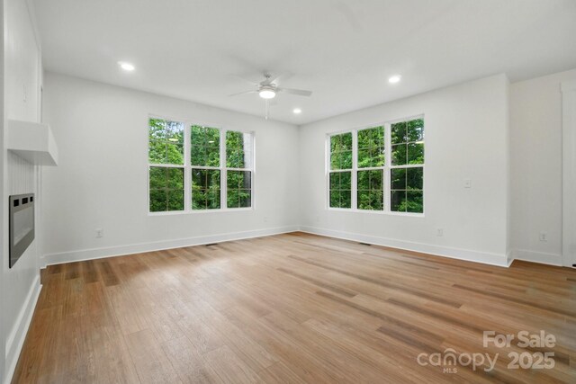 unfurnished living room with a ceiling fan, baseboards, a glass covered fireplace, and light wood-style flooring