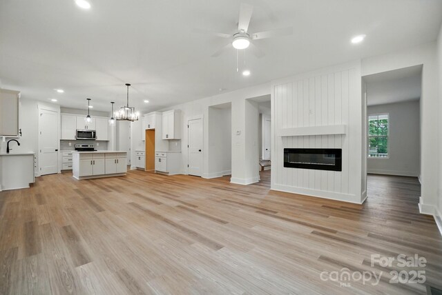 unfurnished living room featuring recessed lighting, a sink, light wood-style flooring, and ceiling fan with notable chandelier
