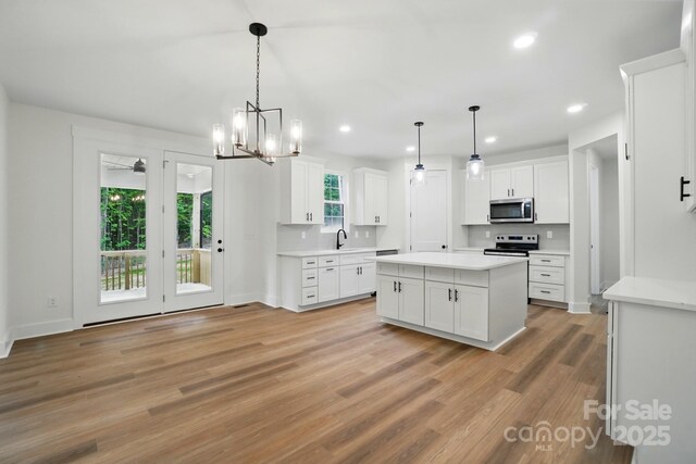 kitchen featuring an inviting chandelier, a sink, light wood-style flooring, stainless steel appliances, and white cabinetry