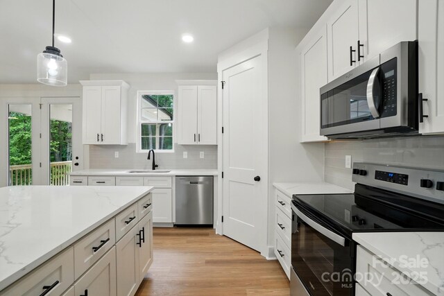 kitchen featuring white cabinets, appliances with stainless steel finishes, a sink, decorative backsplash, and pendant lighting