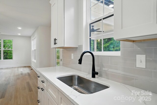 kitchen with white cabinets, light stone countertops, a sink, wood finished floors, and tasteful backsplash