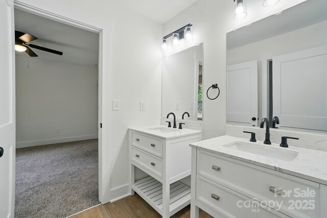 bathroom featuring a sink, baseboards, a ceiling fan, and two vanities
