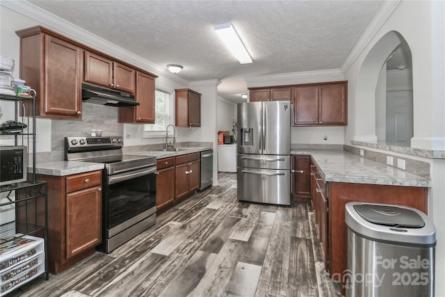 kitchen featuring dark wood-style flooring, crown molding, a sink, under cabinet range hood, and stainless steel appliances