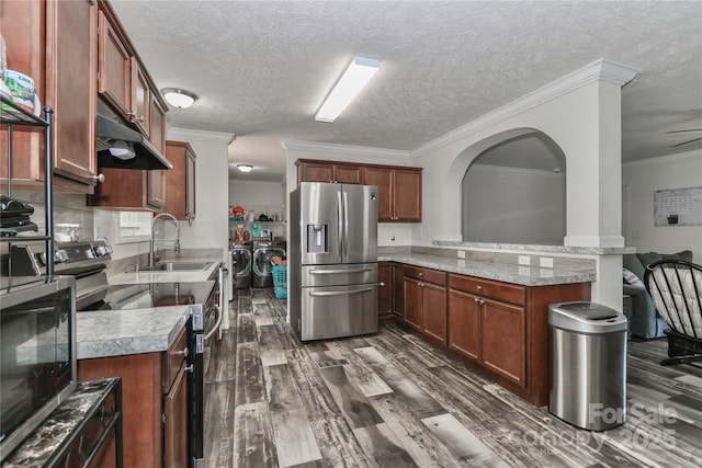 kitchen featuring a peninsula, under cabinet range hood, washing machine and clothes dryer, a sink, and stainless steel appliances