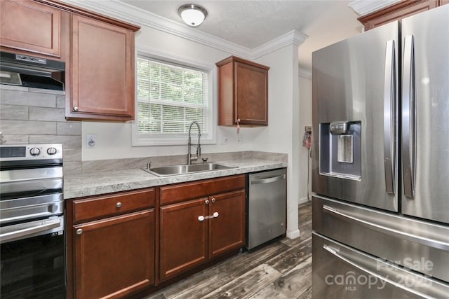 kitchen with crown molding, light countertops, under cabinet range hood, a sink, and appliances with stainless steel finishes