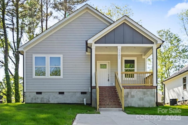 bungalow featuring covered porch, a front yard, cooling unit, board and batten siding, and crawl space