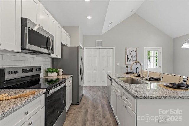 kitchen featuring decorative backsplash, wood finished floors, white cabinets, a sink, and appliances with stainless steel finishes