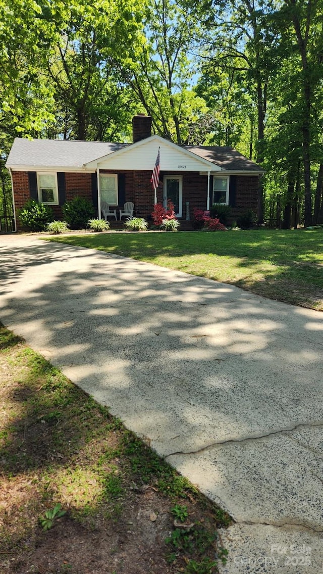 single story home with a chimney, concrete driveway, and a front yard