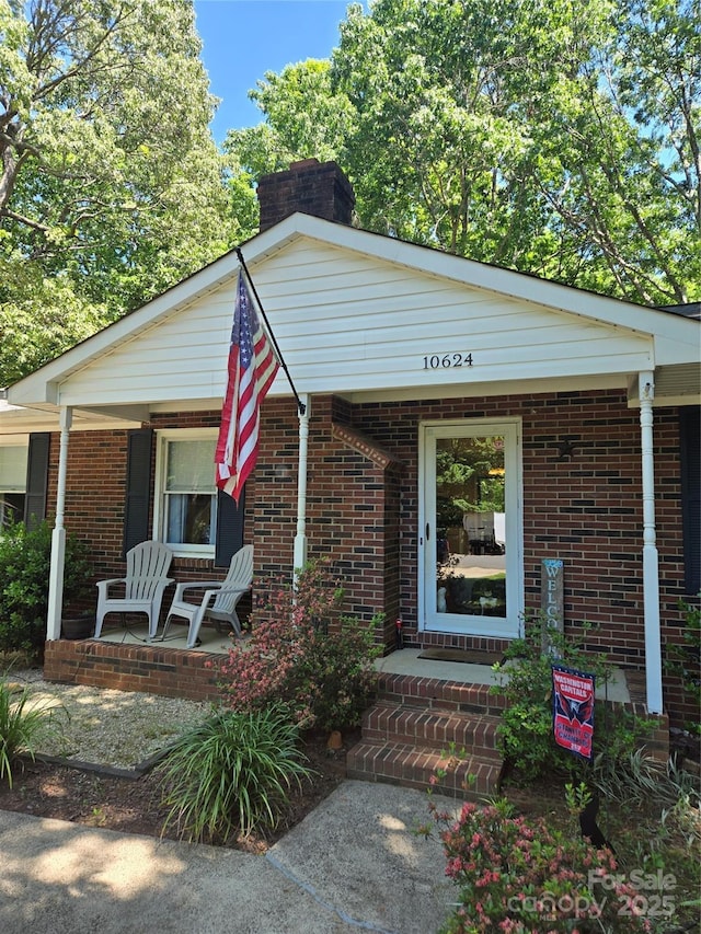 view of front facade featuring covered porch, brick siding, and a chimney