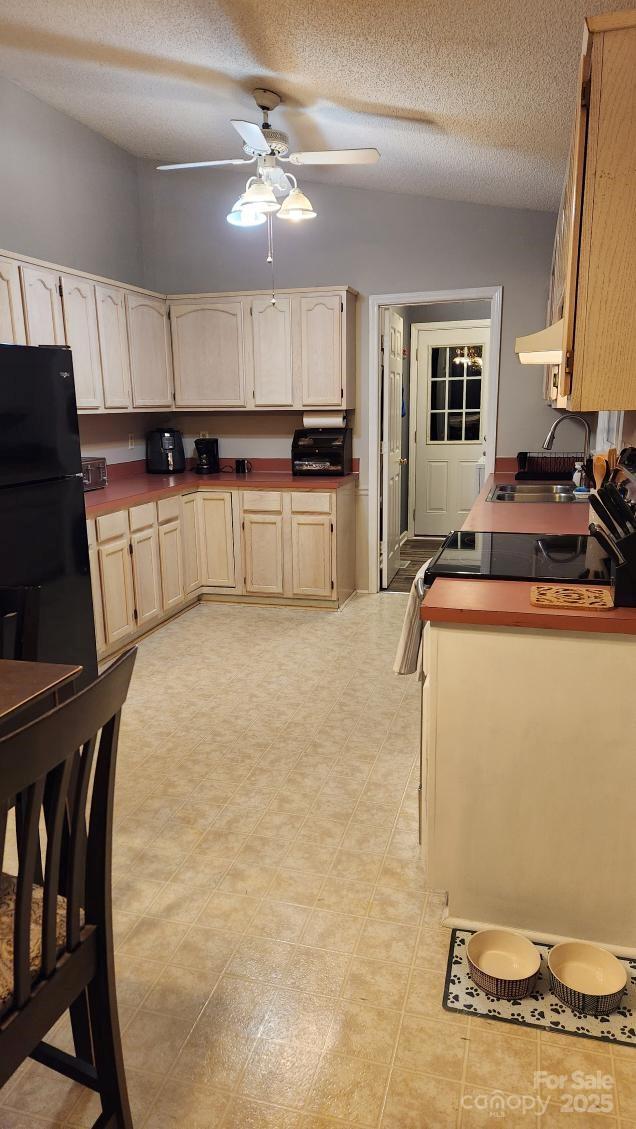 kitchen with a sink, a ceiling fan, a textured ceiling, and under cabinet range hood