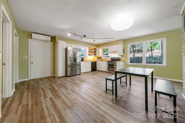 kitchen featuring appliances with stainless steel finishes, an AC wall unit, white cabinets, light countertops, and a textured ceiling