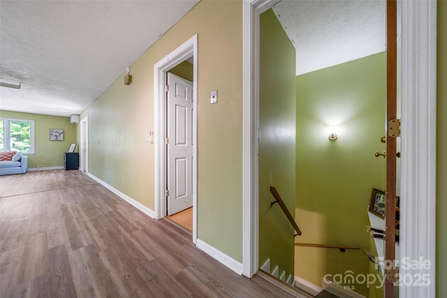 hall featuring a textured ceiling, wood finished floors, baseboards, and an upstairs landing