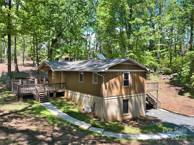 view of side of home featuring stairway, a deck, a shingled roof, and brick siding