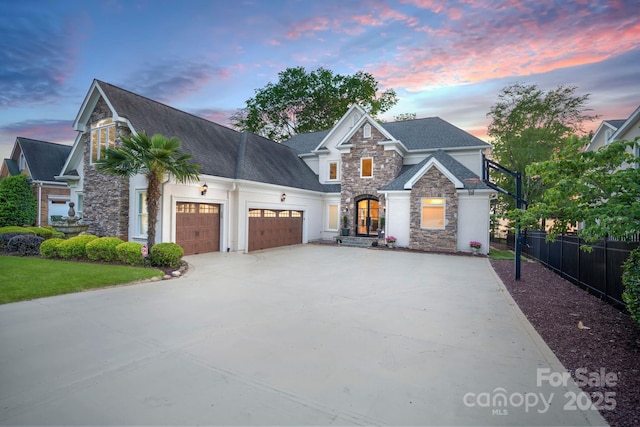 view of front of house with fence, an attached garage, a shingled roof, stone siding, and concrete driveway