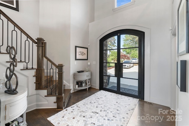 foyer entrance with dark wood-type flooring, stairs, a towering ceiling, and a wealth of natural light