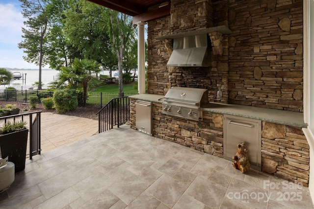 view of patio featuring area for grilling, an outdoor kitchen, fence, and a water view
