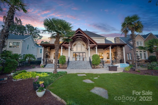 back of house at dusk featuring stone siding, a patio, stucco siding, a chimney, and a yard