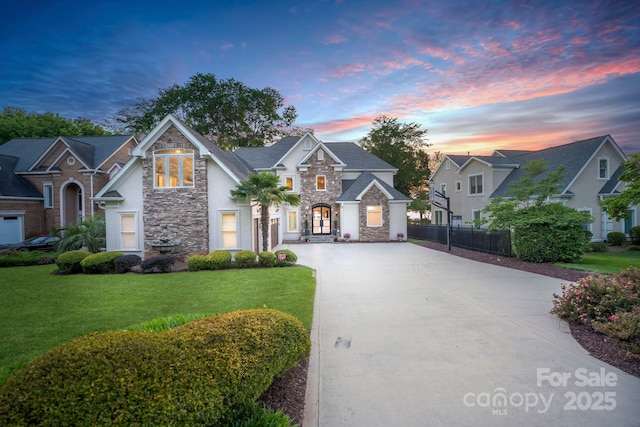 view of front facade featuring a lawn, fence, concrete driveway, and stone siding