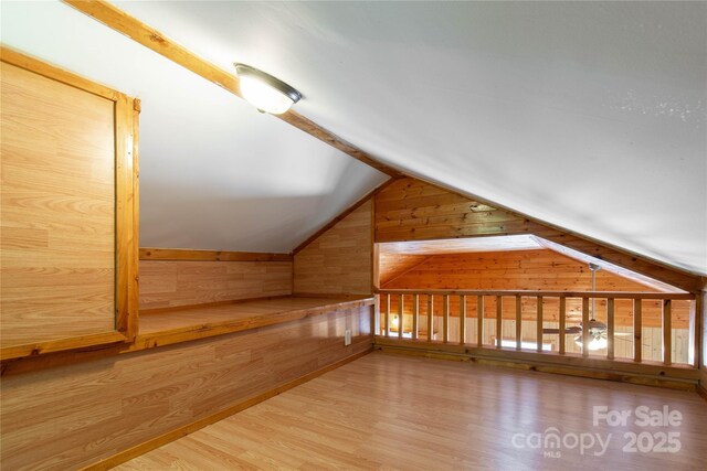 bonus room featuring wood walls, vaulted ceiling, and wood finished floors