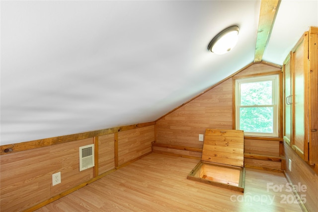 additional living space with vaulted ceiling, wooden walls, and light wood-type flooring