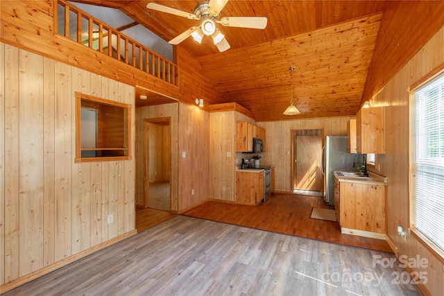 kitchen featuring appliances with stainless steel finishes, a sink, wooden walls, light countertops, and light wood-style floors