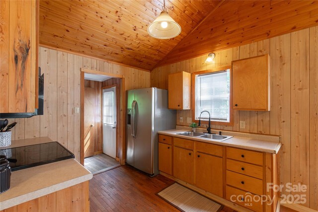 kitchen featuring stainless steel fridge with ice dispenser, a sink, lofted ceiling, light countertops, and wood walls