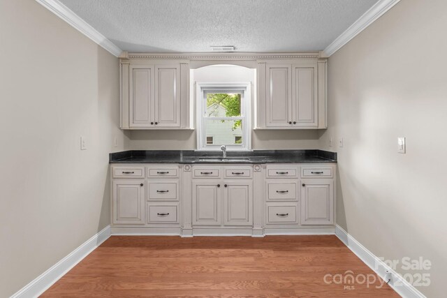 kitchen with light wood-style floors, a sink, a textured ceiling, and dark countertops