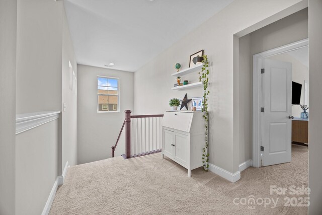 hallway featuring baseboards, an upstairs landing, and carpet