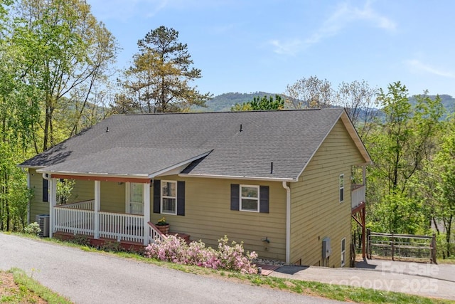 view of front of home with a porch, roof with shingles, and central air condition unit