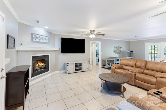 living room with visible vents, crown molding, light tile patterned flooring, ceiling fan, and a warm lit fireplace