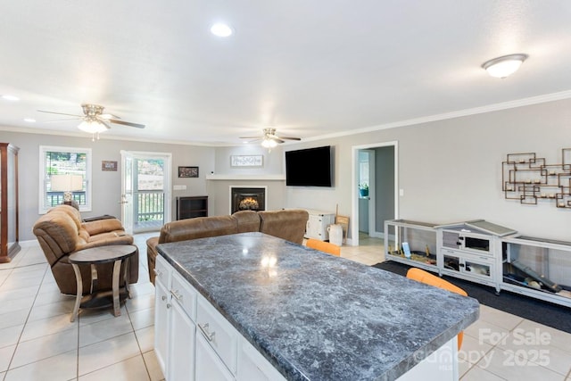 kitchen featuring light tile patterned floors, ceiling fan, a warm lit fireplace, and open floor plan