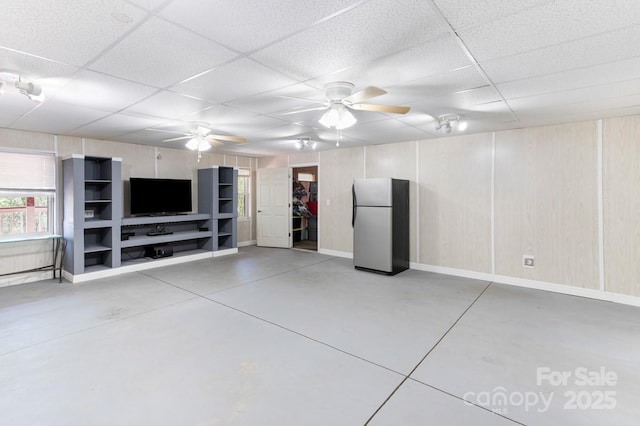 unfurnished living room featuring baseboards, a ceiling fan, a drop ceiling, and concrete floors