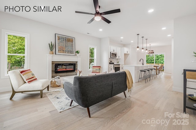 living room with recessed lighting, light wood-style flooring, baseboards, and a glass covered fireplace