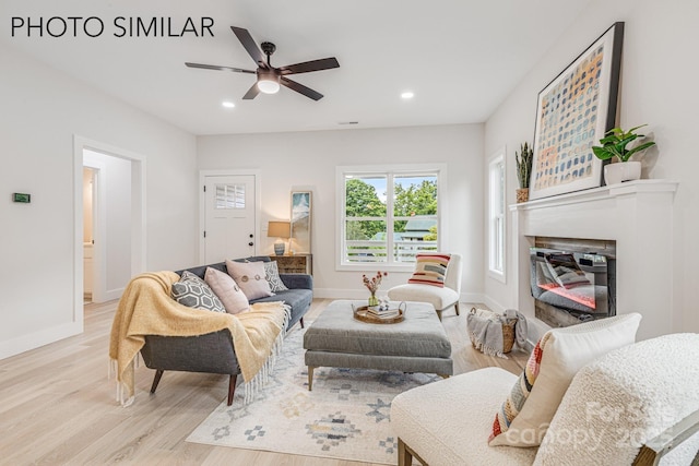 living area featuring a ceiling fan, light wood-type flooring, baseboards, a glass covered fireplace, and recessed lighting