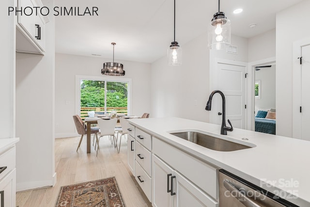 kitchen with light wood finished floors, white cabinetry, decorative light fixtures, and a sink