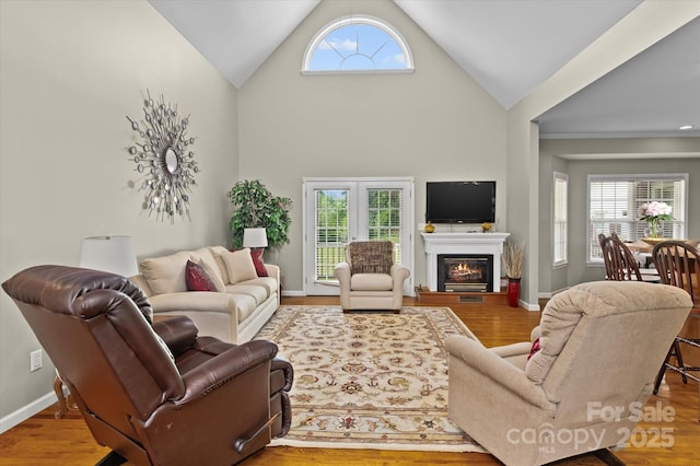 living area with a glass covered fireplace, baseboards, vaulted ceiling, and wood finished floors