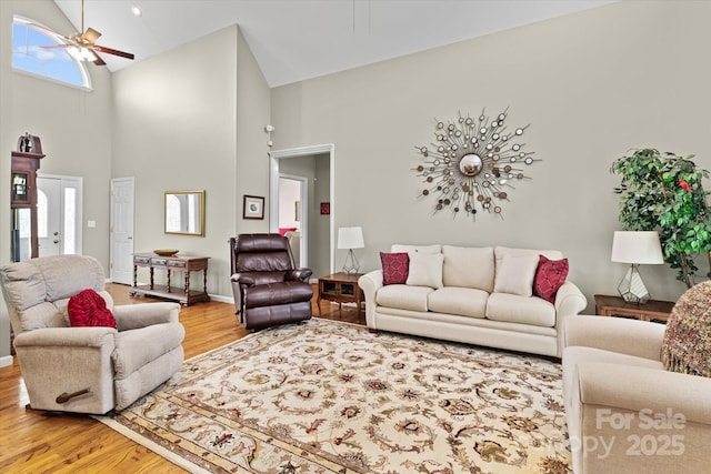 living area featuring light wood-style floors, baseboards, ceiling fan, and high vaulted ceiling