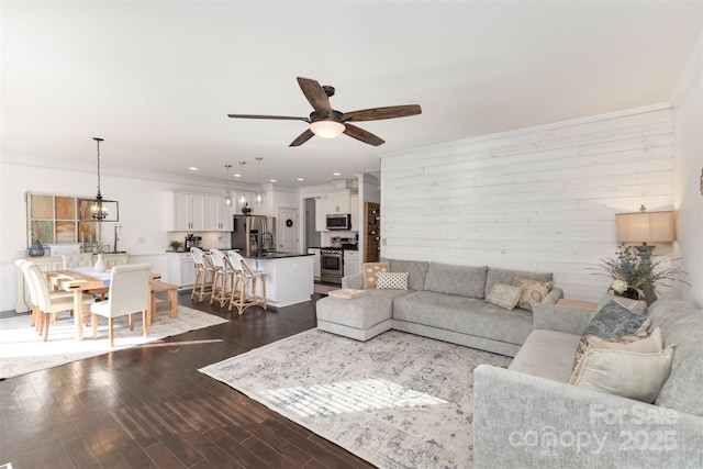 living area featuring a ceiling fan, crown molding, dark wood-style floors, wooden walls, and recessed lighting