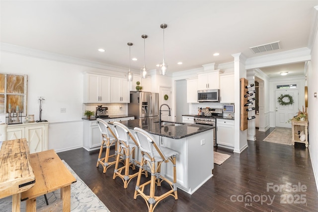 kitchen featuring visible vents, a kitchen island with sink, a breakfast bar, a sink, and stainless steel appliances