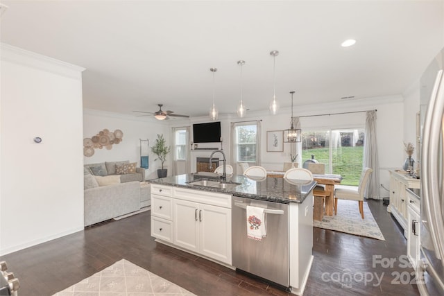 kitchen with ornamental molding, open floor plan, dark stone counters, a sink, and appliances with stainless steel finishes