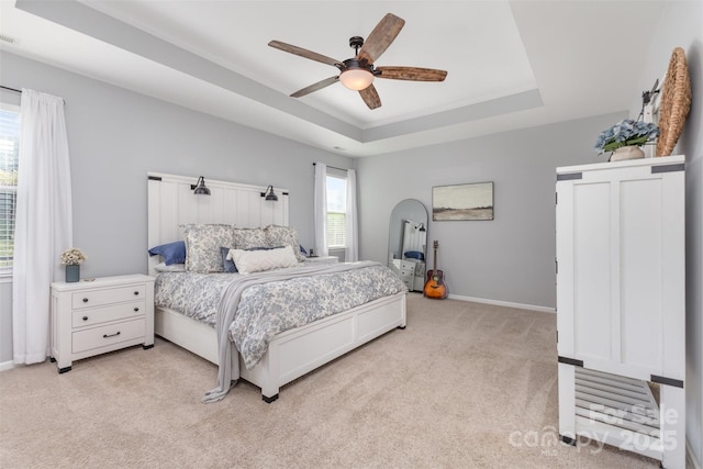 bedroom with baseboards, a raised ceiling, ceiling fan, and light carpet