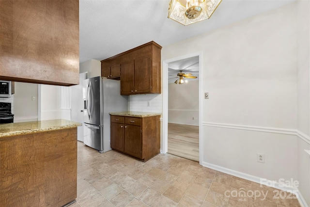 kitchen with ceiling fan, light stone counters, stainless steel fridge, black electric range oven, and baseboards