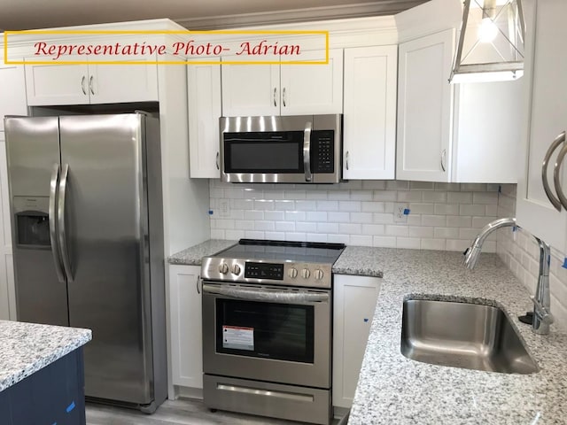kitchen with backsplash, stainless steel appliances, white cabinetry, and a sink