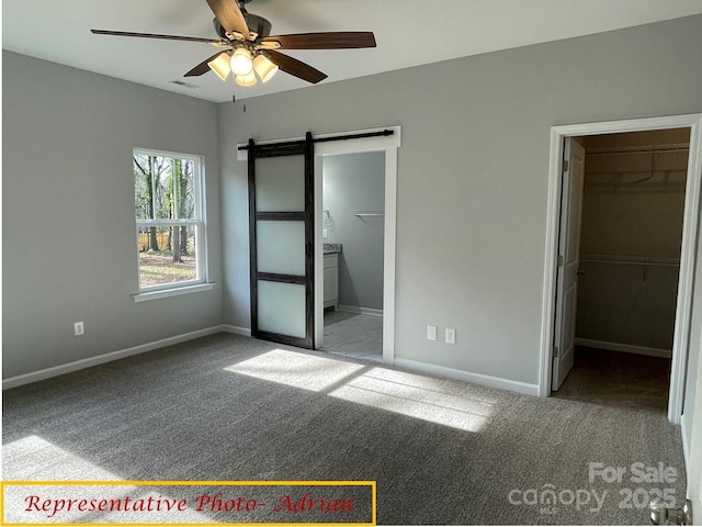 unfurnished bedroom with baseboards, a barn door, carpet, and a spacious closet