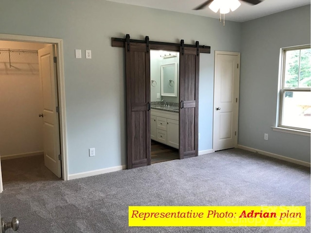 unfurnished bedroom featuring a barn door, a walk in closet, carpet, baseboards, and ensuite bathroom