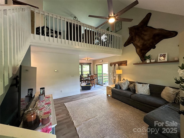living room featuring a ceiling fan, baseboards, wood finished floors, and a towering ceiling